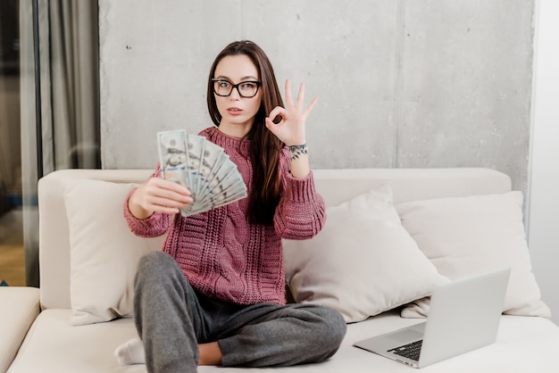 Frau, die zu Hause Geld auf einer Couch mit Laptop verdient