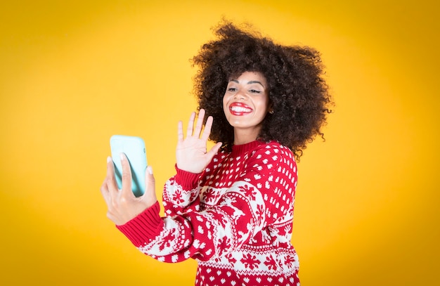 Frau, die zu Weihnachten über Handy-Videoanruf spricht, gelber Hintergrund