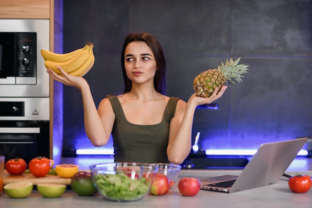 Frau, die zwischen Nachtisch und Früchten am Tisch in der Küche wählt. Gesunde Ernährung