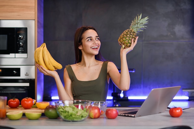 Frau, die zwischen Nachtisch und Früchten am Tisch in der Küche wählt. Gesunde Ernährung