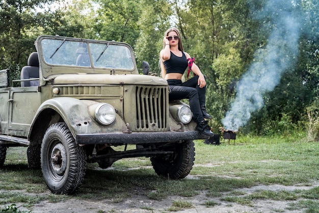 Frau draußen sitzt auf Motorhaube des Militärautos