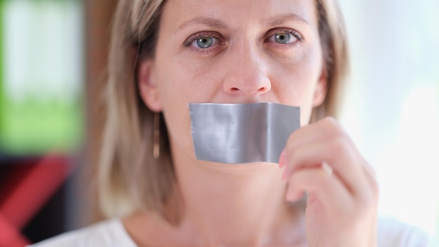 Frau entfernt Klebeband von ihrem Mund, Nahaufnahme, um Freiheit zu erlangen und das Zensurkonzept zu stoppen