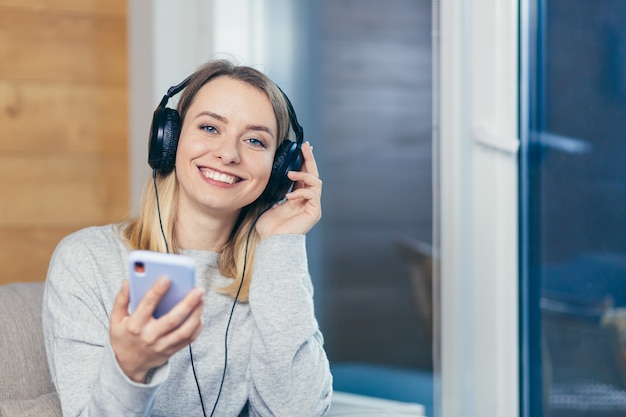 Frau entspannt sich zu Hause und hört Musik mit großen Kopfhörern benutzt Handy
