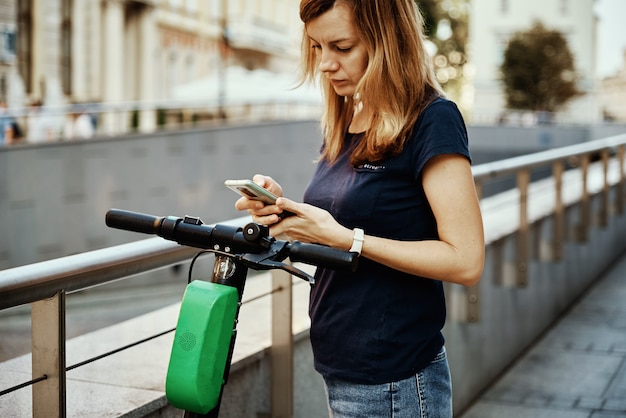 Frau entsperrt Elektroroller zur Miete mit der Handy-App. Moderner urbaner Ökoverkehr