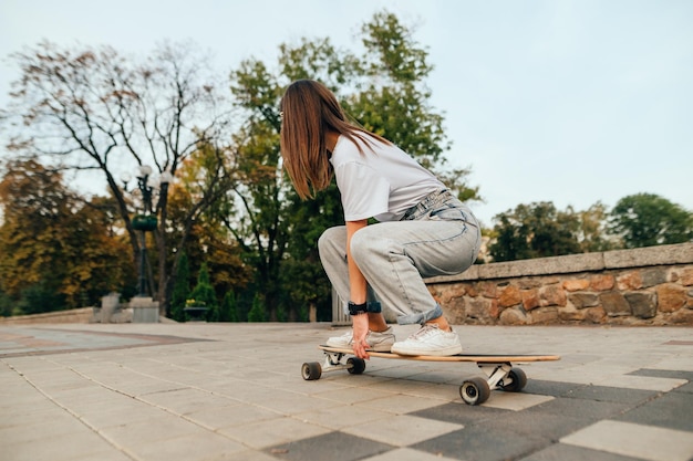 frau fährt ihr skateboard und macht tricks auf einem betonpflaster in der nähe des stadtparks