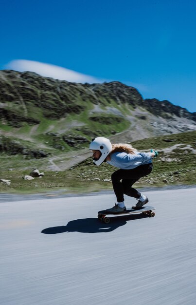 Frau fährt Skateboard und macht Tricks zwischen den Kurven auf einem Bergpass