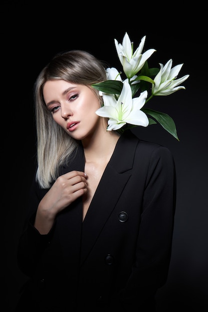 Frau färbte Haarfarbe einer Blondine mit Lilienblume auf schwarzem Hintergrund. Färbendes Haarfrauenmodell in der Aschefarbe