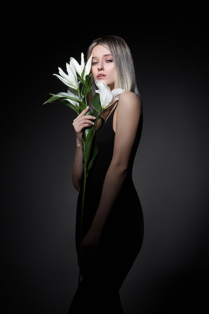 Frau färbte Haarfarbe einer Blondine mit Lilienblume auf schwarzem Hintergrund.