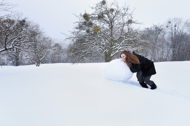 Frau formt einen großen Schneemann aus dem Schnee