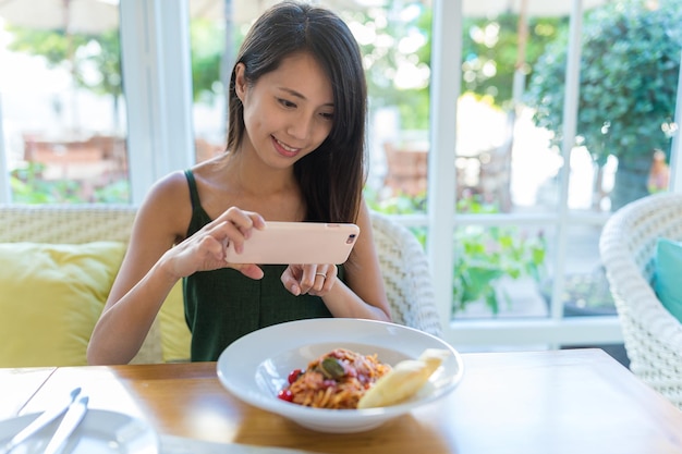 Frau fotografiert mit Handy auf ihrem Teller im Restaurant