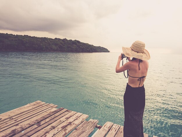 Foto frau fotografiert, während sie auf dem pier gegen den himmel steht