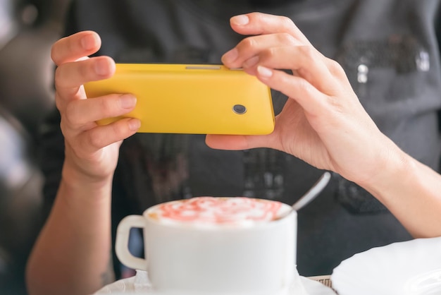 Frau fotografierte Tasse Kaffee auf einem gelben Smartphone