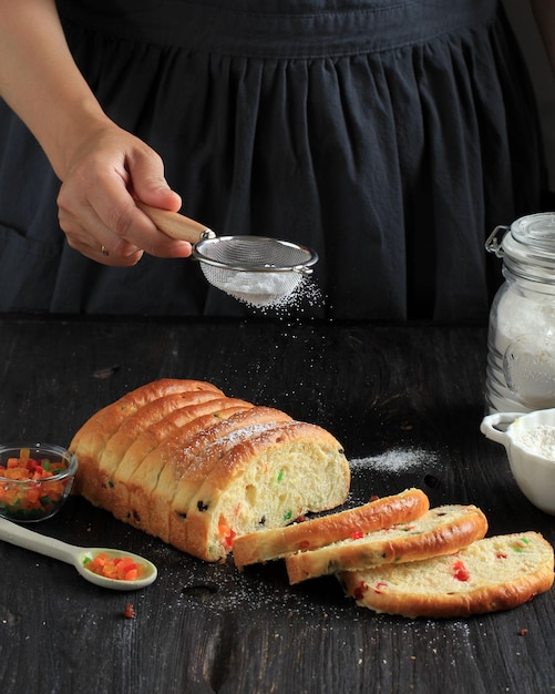 Frau frisch gebackenes Obstbrot mit Puderzucker bestreuen