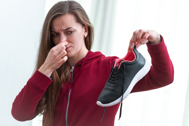 Frau fühlt unangenehmen Geruch von verschwitzten Laufschuhen nach langem Sporttraining und aktivem Lebensstil. Schuhbedarf bei der Reinigung und Geruchsentfernung. Schuhpflege und Glanz