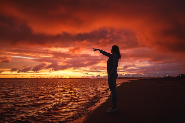 Foto frau geht allein am strand und betrachtet den farbenfrohen sonnenuntergang nach dem regen beine in den weißen schuhen rot-orange-purpur-lila-farben
