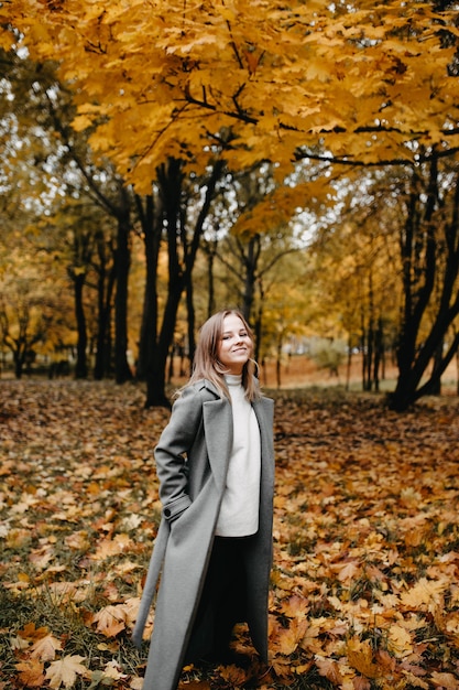 Frau geht durch die Herbstallee des Parks ein Mädchen in einem grauen Mantel