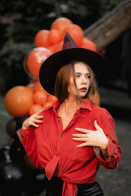 Frau gekleidet als Hexe für Halloween Orange Kugeln auf dem Hintergrund des Wald-Halloween-Party-Kunstdesigns