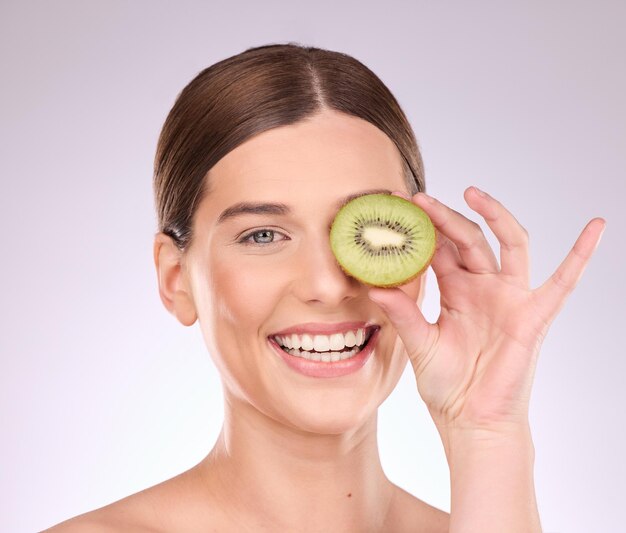 Frau Gesicht und Hand mit Kiwi für Hautpflege Ernährung oder gesunde Ernährung vor grauem Studiohintergrund Porträt eines glücklichen weiblichen Lächelns mit Früchten für organische Gesichtsbehandlung oder Naturkosmetik
