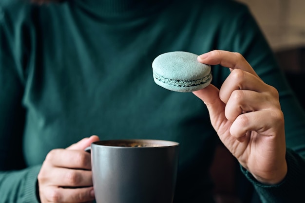 Frau gesichtslos mit Kaffeetasse und Makronen sitzt am Cafétisch Nahaufnahme Selektiver Fokus