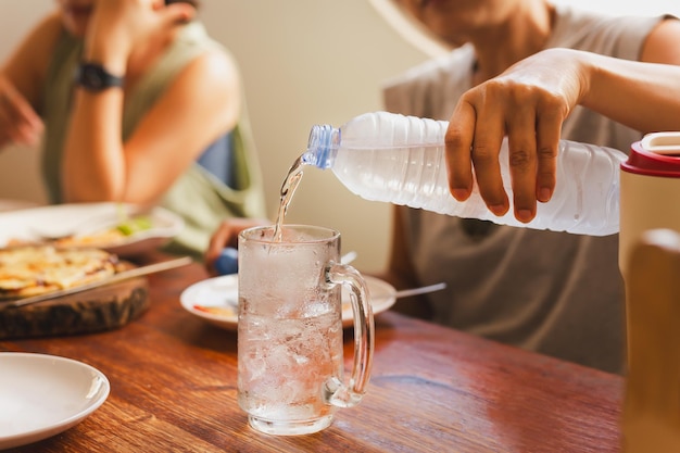 Frau gießt am Esstisch kaltes Wasser aus der Flasche ins Glas