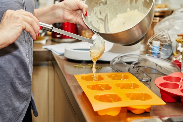 Frau gießt den teig in muffinformen für die herstellung von sonnengetrockneten tomatenmuffins.