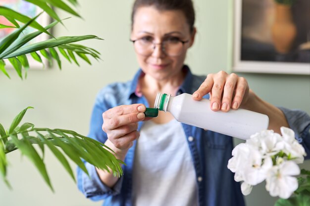 Frau gießt flüssigen Mineraldünger. Anbau und Pflege von Zimmerpflanzen. Hobbys und Freizeit, Gartenarbeit, Zimmerpflanze, Großstadtdschungel in der Wohnung