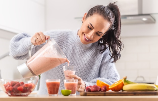 Frau gießt Frucht-Smoothie in Tassen in einer Küche.