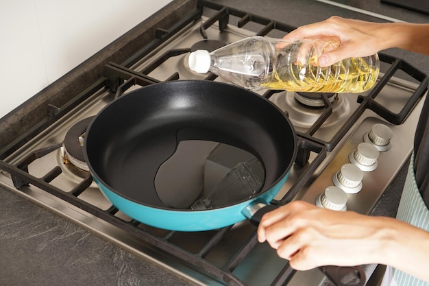 Frau gießt Öl aus der Flasche in die Pfanne in der Küche Hausmannskost