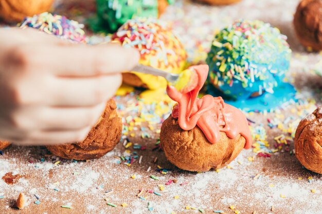 Frau gießt orange Zuckerguss auf einem Donut.