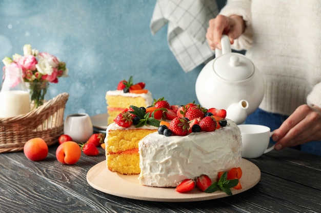 Frau gießt Tee auf Holztisch mit Beerencremekuchen. Leckeres Dessert