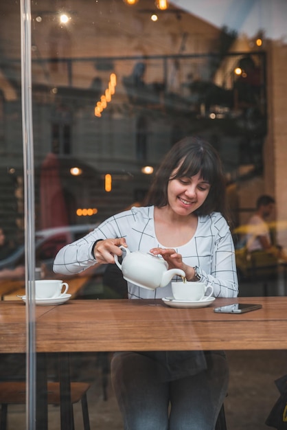 Frau gießt Tee in die Tasse im Café