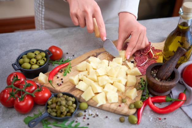 Frau hackt Parmesankäse mit Messer auf grauem Tisch in der heimischen Küche