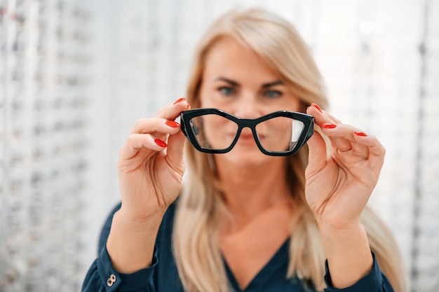 Frau hält Brille in Händen und steht im Laden