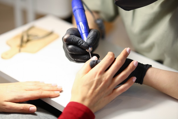 Frau hält die Hand des Klienten und verarbeitet die Nagelhaut mit einem speziellen Apparat