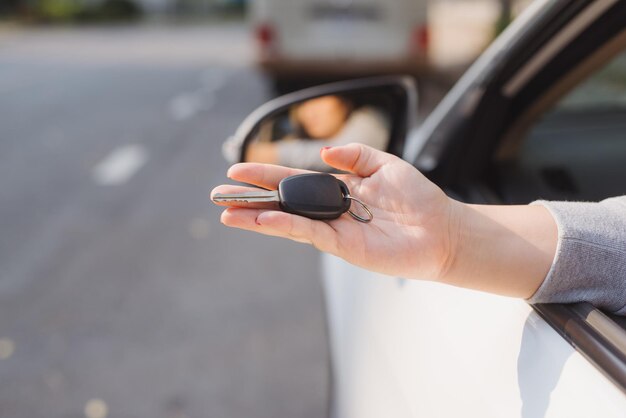 Frau hält die Zündschlüssel eines Autos in der Hand und lässt sie durch das offene Seitenfenster baumeln