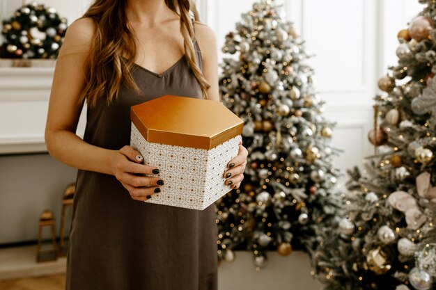 Frau hält ein schön verpacktes Weihnachtsgeschenk in einer goldenen Schachtel