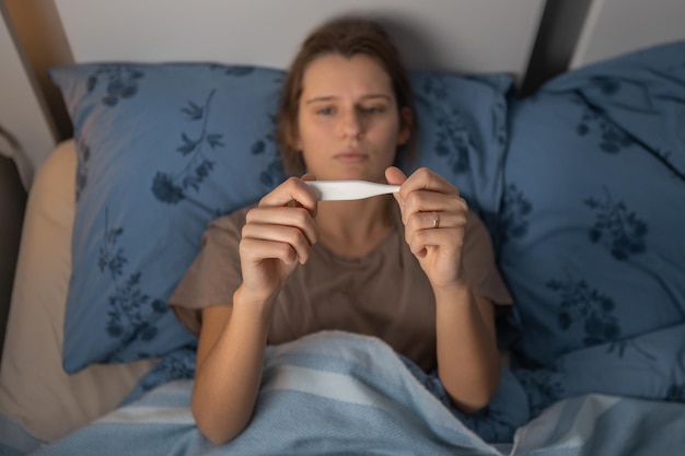 Frau hält ein Thermometer in den Händen und schaut darauf. Frauen, die sich schlecht fühlen, leiden unter Hitzetemperatur