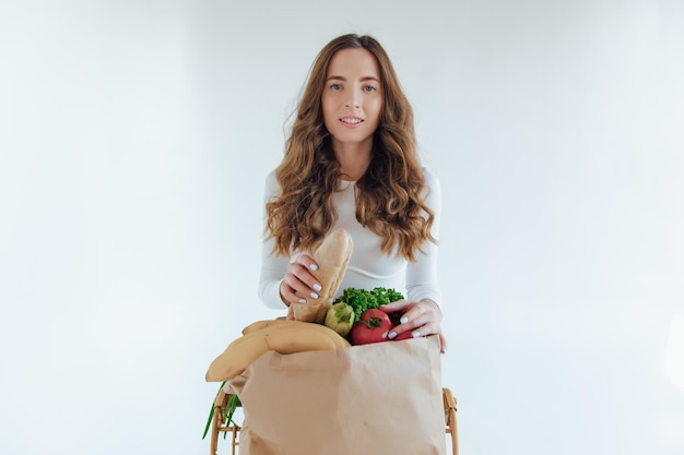 Frau hält eine Einkaufstasche voller Lebensmittel, Mango, Salat, Rettich, Zitrone, Karotten auf weißem Hintergrund