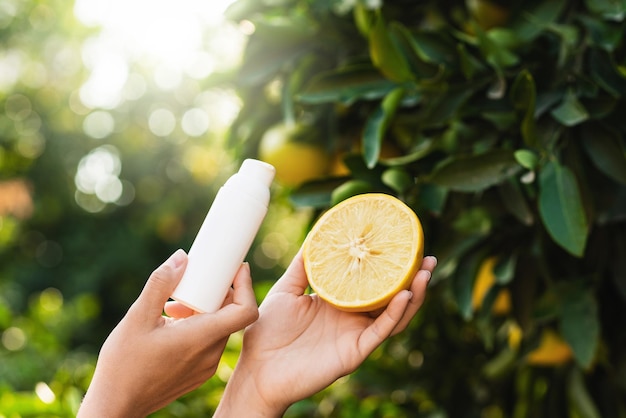 Frau hält eine Flasche Hautpflegeprodukt und die Hälfte der Zitrone in ihren Händen auf Zitronenbaumhintergrund
