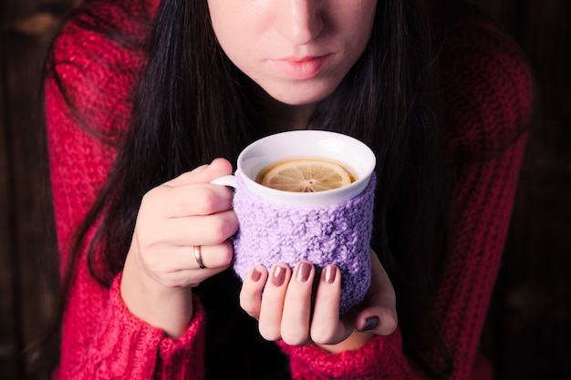 Frau hält eine gestrickte Tasse Tee mit Zitrone