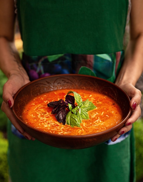 Frau hält eine irdene Schüssel mit Tomatencremesuppe.