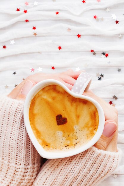 Frau hält eine Tasse heißen Kaffee mit Zimtherzen.