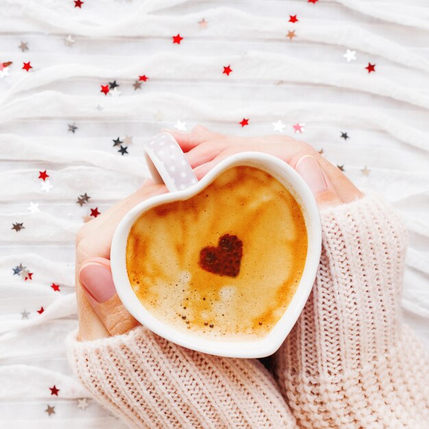 Frau hält eine Tasse heißen Kaffee mit Zimtherzen