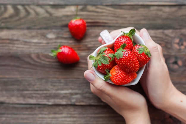 Frau hält eine Tasse voller Erdbeeren in Händen.