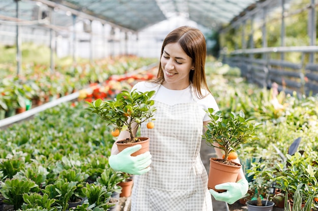 Frau hält einen Blumentopf in ihren Händen, der Pflanzen zum Verkauf anpflanzt, als Geschenk Blumen in einer Topfpflanze im Gewächshaus