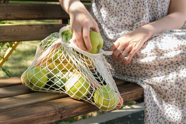 Frau hält einen grünen Apfel in der Hand Gestrickte Netztasche mit Gemüse und Obst