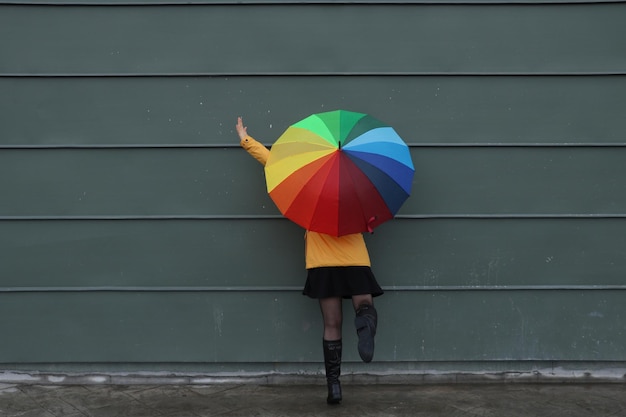 Foto frau hält einen regenschirm, während sie an der wand steht