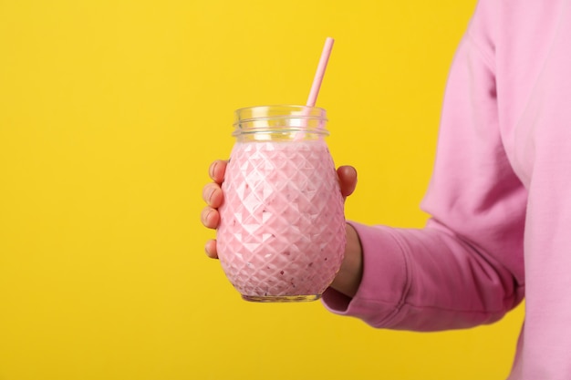 Frau hält Glas Erdbeermilchshake auf gelb