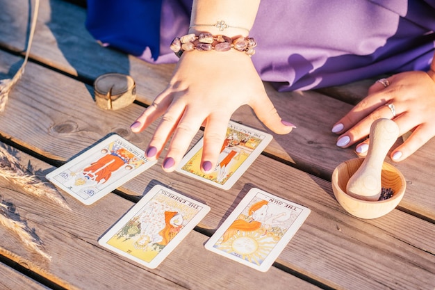 Foto frau hält ihre hand mit lila nägeln über vier tarotkarten, die auf einer holzoberfläche neben ährchen und lavendel ausgebreitet sind. minsk, weißrussland - 28.07.2021