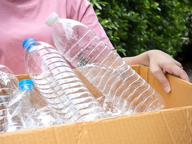 Frau hält Kiste mit Plastikflaschenmüll in der Hand, um sie zu recyceln